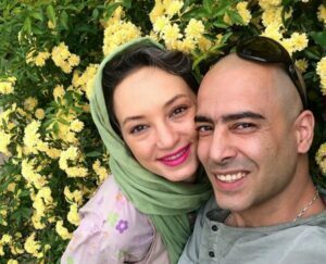 نیما فلاح با تیشرت طوسی و همسرش سحر ولدبیگی در کنار گلها
