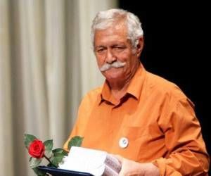 آتش تقی پور از بازیگران مرد قد بلند ایرانی با پیراهن نارنجی و گل و تقدیر نامه در دستش